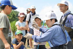 三春ダムの本川（大滝根川）に住む水生生物を観察しました。<br />子供たちは網を持って、水草や石の間をガサガサと足で誘き寄せていました。<br />時折、オイカワが群れになって足元を泳いでいく姿を見ることが出来ました。<br />ヤゴやシジミ、ドジョウやブラックバスの稚魚などたくさんの水生生物が見られました。<br />漁協の協力で投網も投げていただきました。オイカワやハヤの他に50cm以上のニゴイも網に掛かり子供たちは驚いていました。<br />最後に大滝根川に住んでいる水生生物の特徴や今日捕った魚やヤゴなどの飼い方などをインストラクターの先生から教えていただきました。